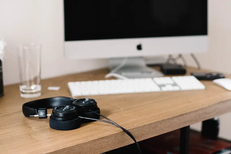 Audífonos sobre un escritorio de madera junto a una computadora y un teclado blanco