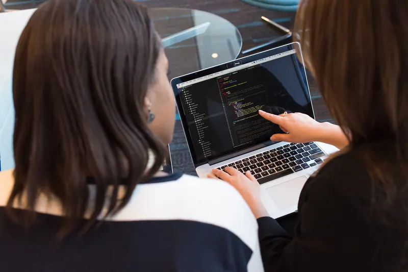 Dos mujeres revisando código en la pantalla de una laptop