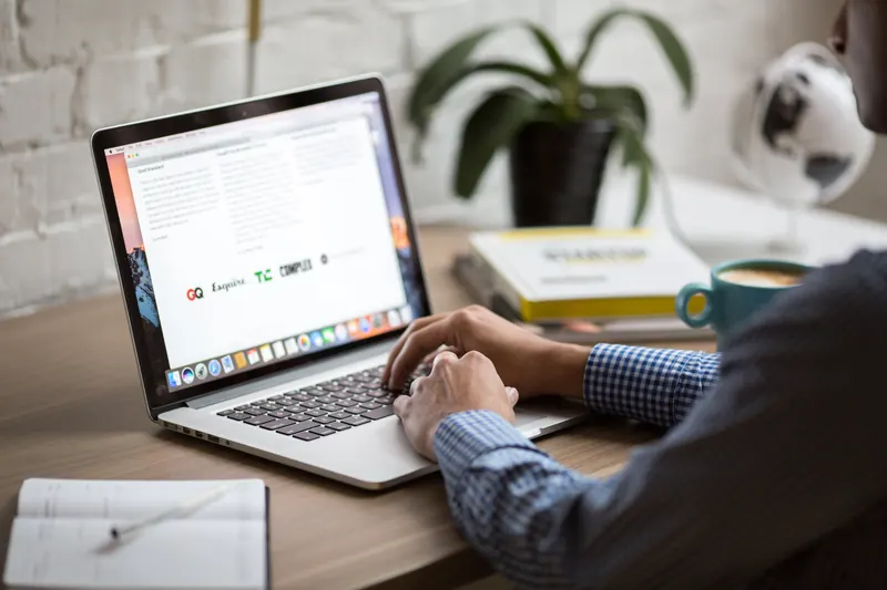 Hombre escribiendo en una laptop sobre un escritorio con taza, libros, planta y un globo terráqueo
