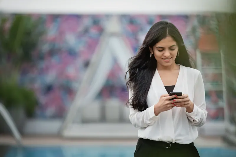 Mujer con blusa blanca sonriendo mientras escribe un mensaje en su teléfono móvil