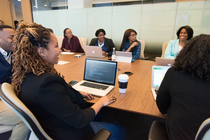 Grupo de personas en una reunión alrededor de una mesa de madera con laptops y café