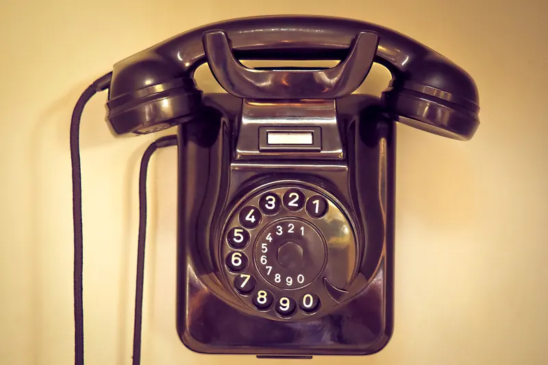 Teléfono antiguo de disco negro colgado en una pared de tono amarillo cálido