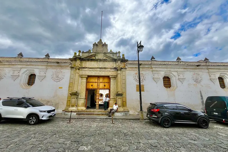 Fachada blanca con portal de piedra y calle empedrada de la Universidad de San Carlos, Antigua Guatemala