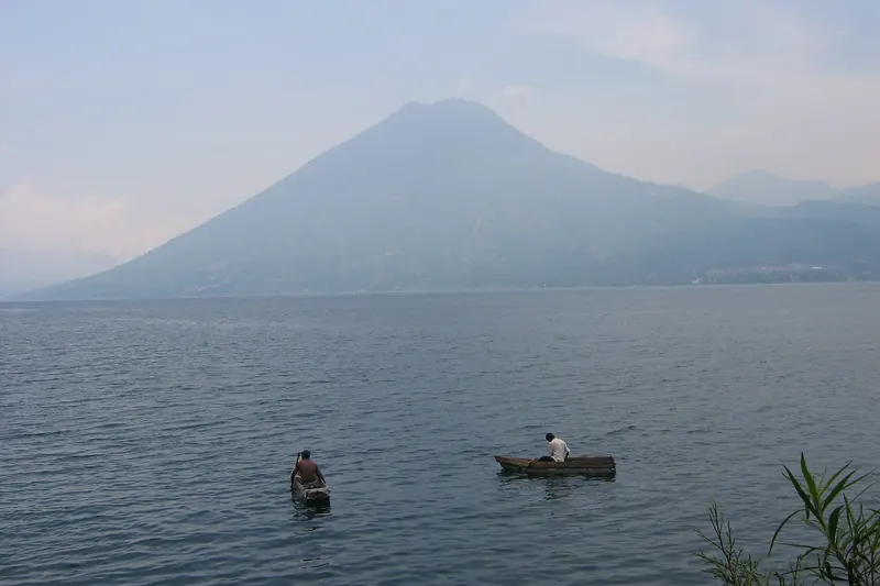 Dos pescadores en pequeñas lanchas sobre el lago de Atitlán con un volcán entre la bruma al fondo