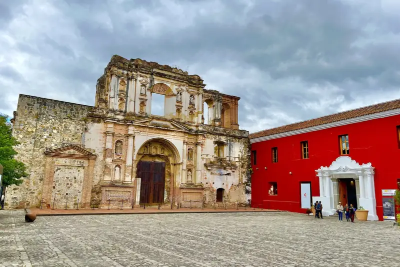 Ruinas de la fachada de la iglesia de la Compañía de Jesús junto a un edificio rojo en Antigua Guatemala