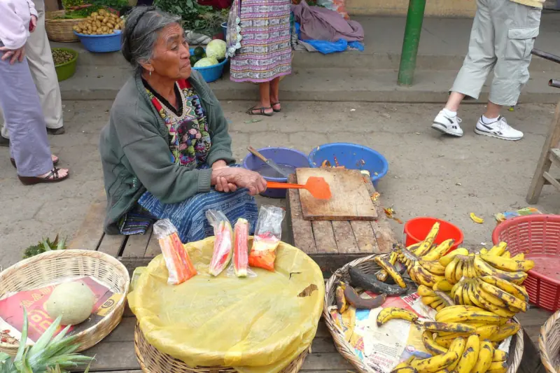 Vendedora sentada junto a canastas con plátanos, frutas y verduras en un mercado de Guatemala