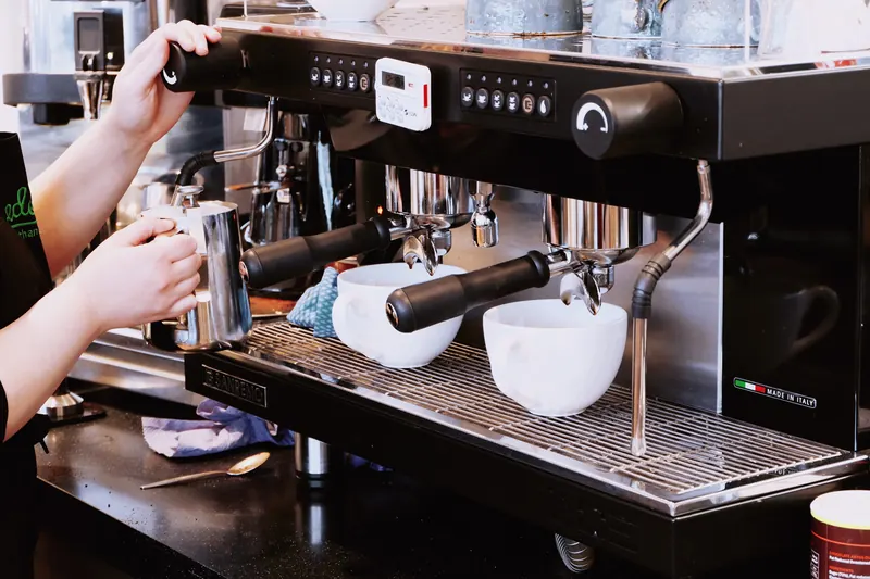 Barista preparando café en una máquina espresso con dos tazas blancas
