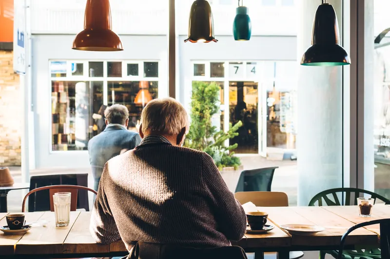Hombre visto de espaldas sentado junto a una ventana en una cafetería con lámparas de colores