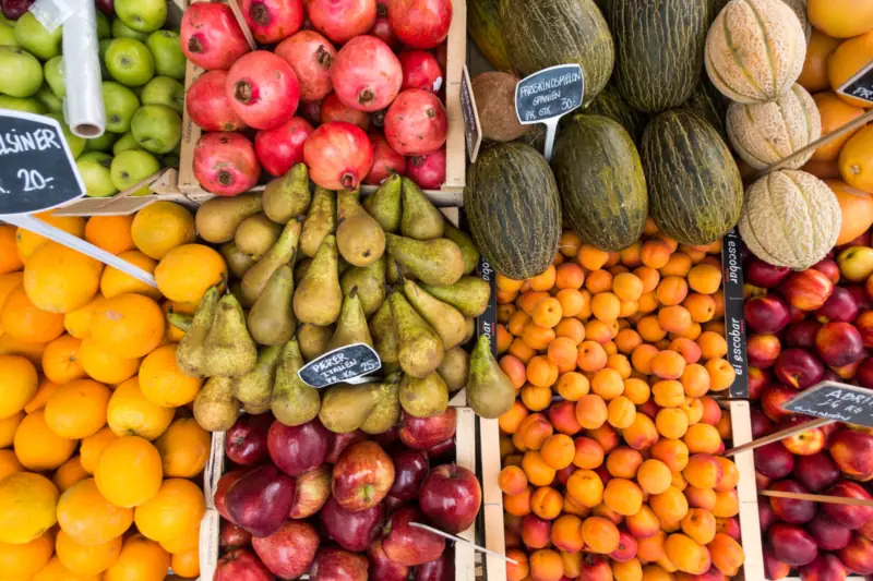 Puesto de frutas con melones, peras, naranjas y granadas ordenados por cajas