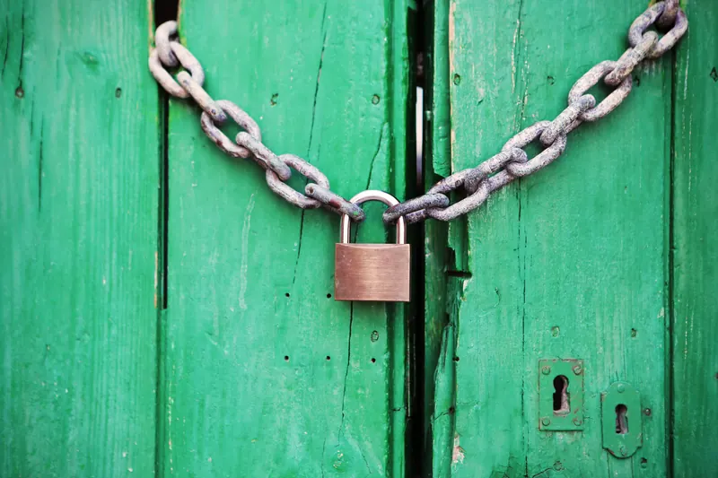 Cadena con un candado cerrando dos puertas de madera verdes