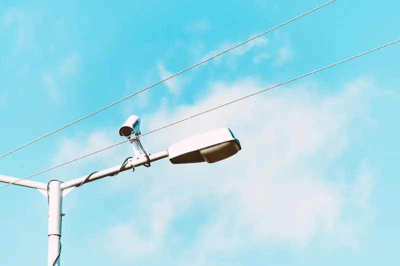 Cámara de seguridad sobre un poste de alumbrado contra un cielo azul con nubes