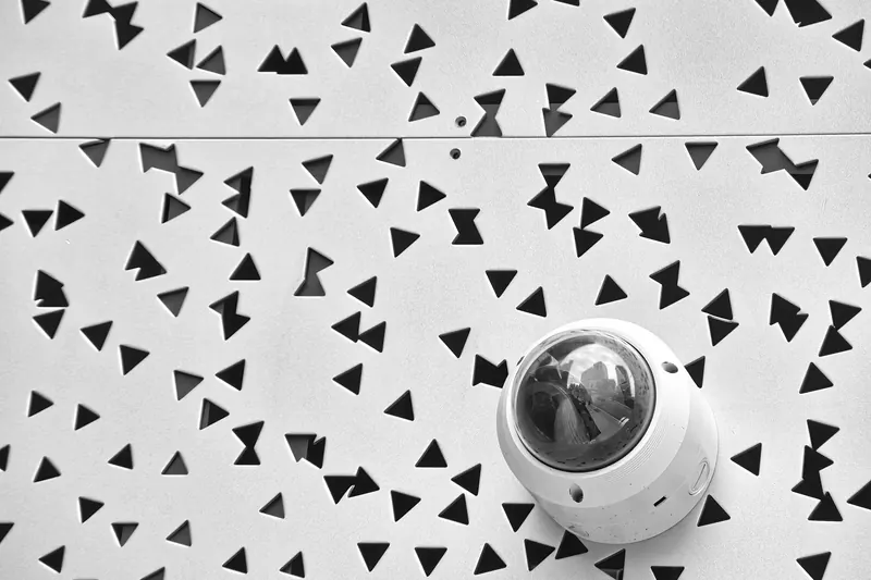 Cámara de vigilancia tipo domo en una pared blanca con perforaciones triangulares