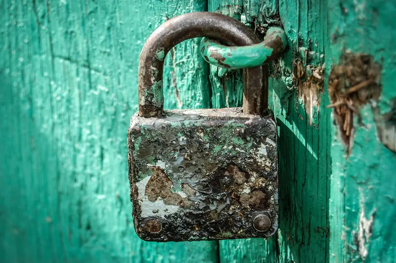 Candado metálico oxidado sujetando una puerta de madera pintada de verde