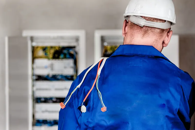 Técnico con casco blanco y overol azul frente a un panel con cables de conexión