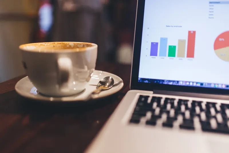 Taza de café junto a una laptop que muestra una gráfica de barras de colores