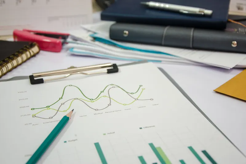 Hojas impresas con gráficas de líneas y barras, un lápiz y cuadernos sobre un escritorio