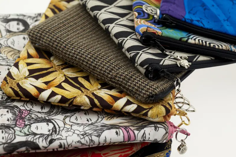 Pila de bolsas de tela artesanales con cierre y estampados de colores, listas para la venta