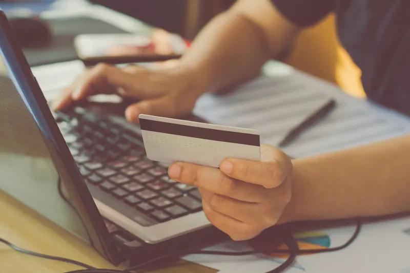 Manos sobre el teclado de una laptop sosteniendo una tarjeta de crédito para pagar