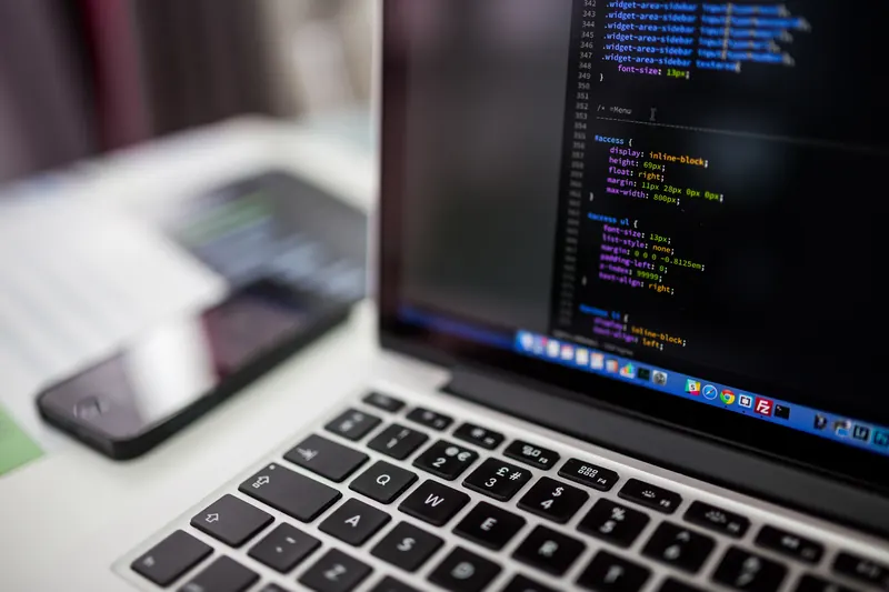 Teclado de laptop y pantalla con código de programación en colores, vista de cerca