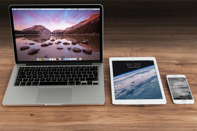 Laptop, tableta y teléfono móvil alineados sobre una mesa de madera, tres pantallas de distinto tamaño